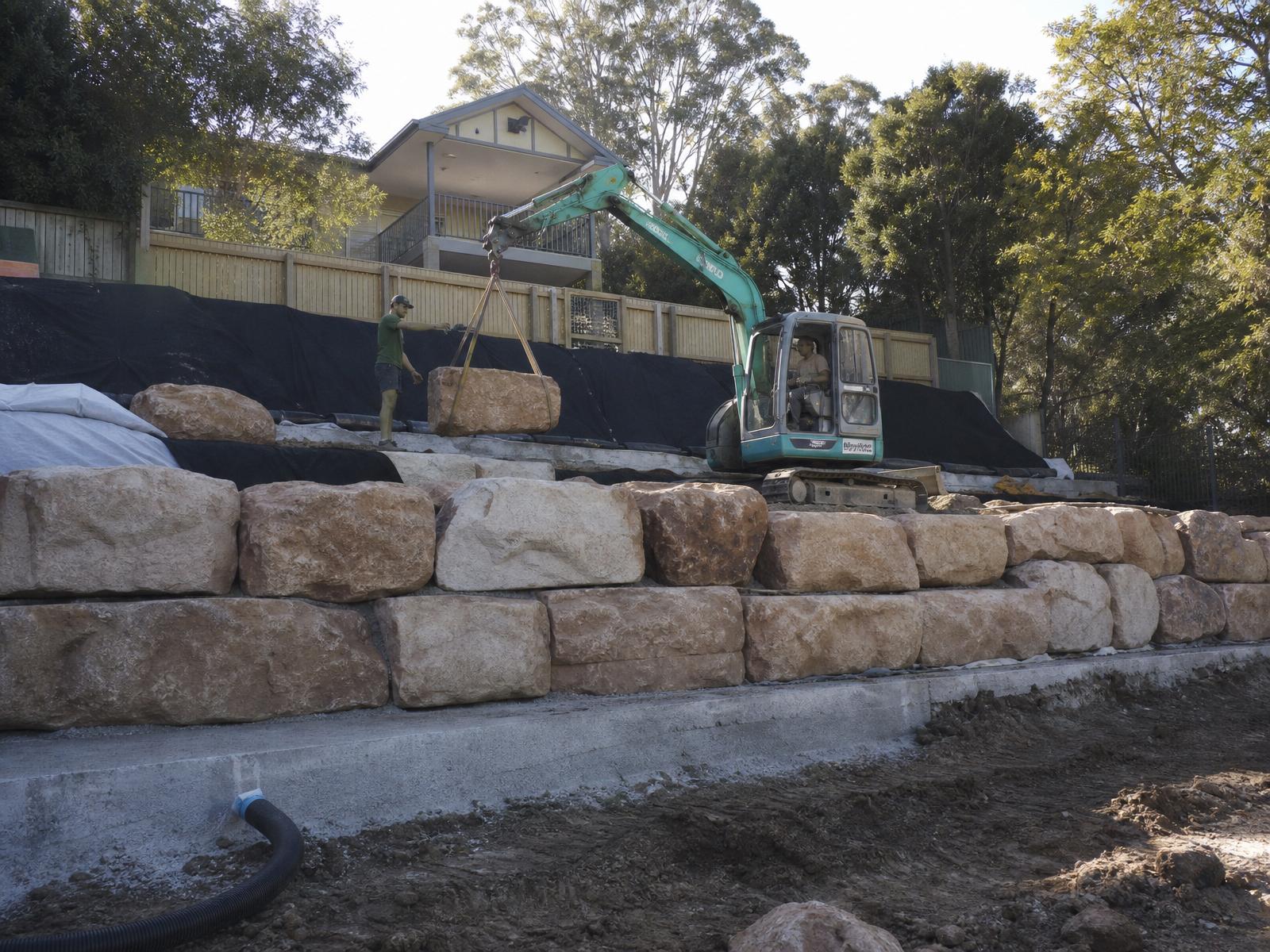 Australian structural landscape works with excavator placing sandstone blocks on a retaining wall