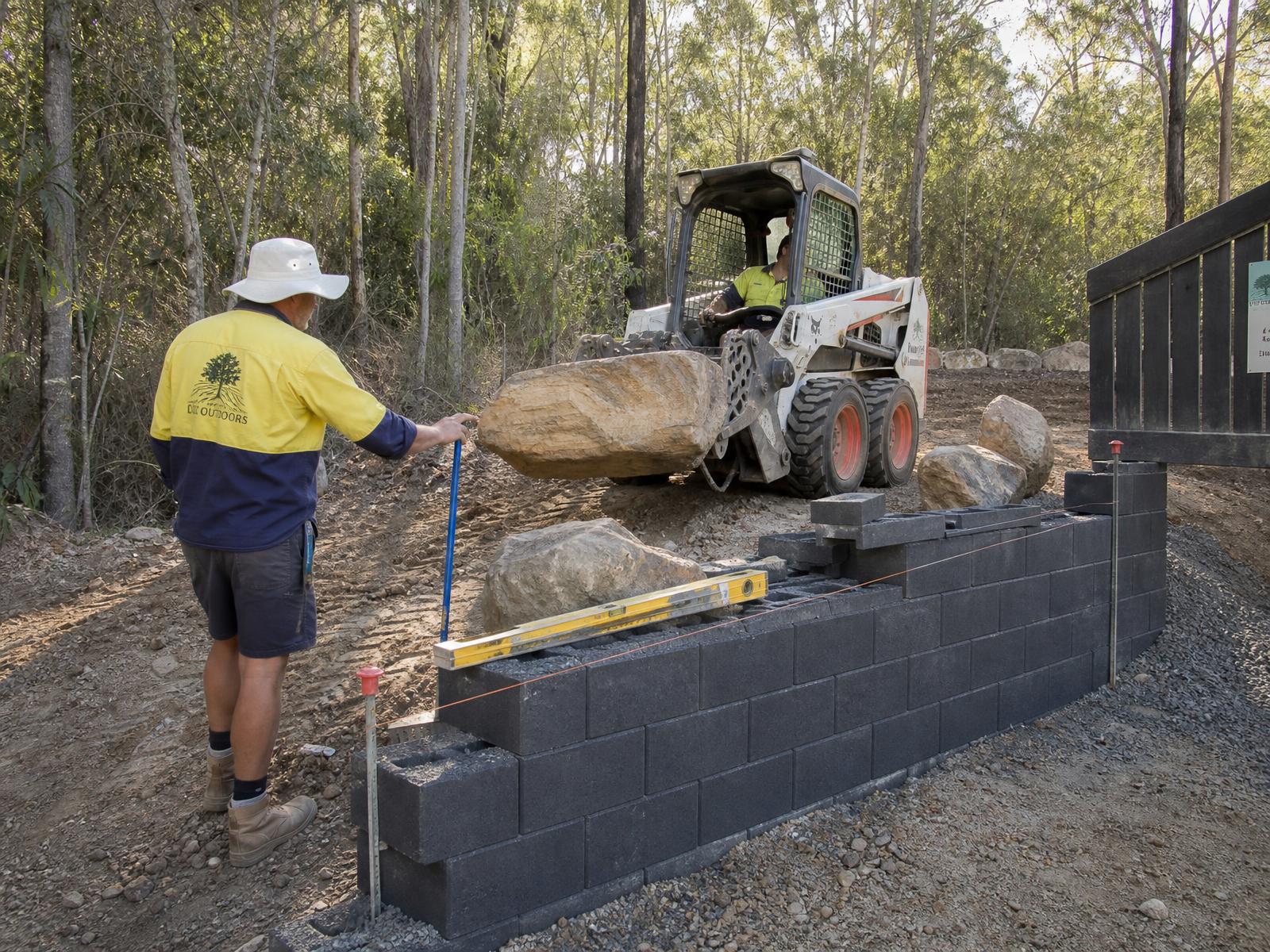 Australian landscape construction site with skid-steer loader and sandstone boulders being placed